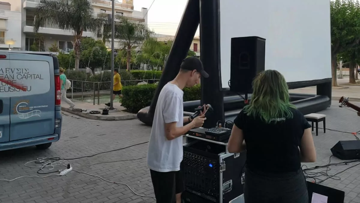 In the image, two volunteers are setting up equipment for an outdoor screening, with a large inflatable screen and the solar cinema  van parked nearby.