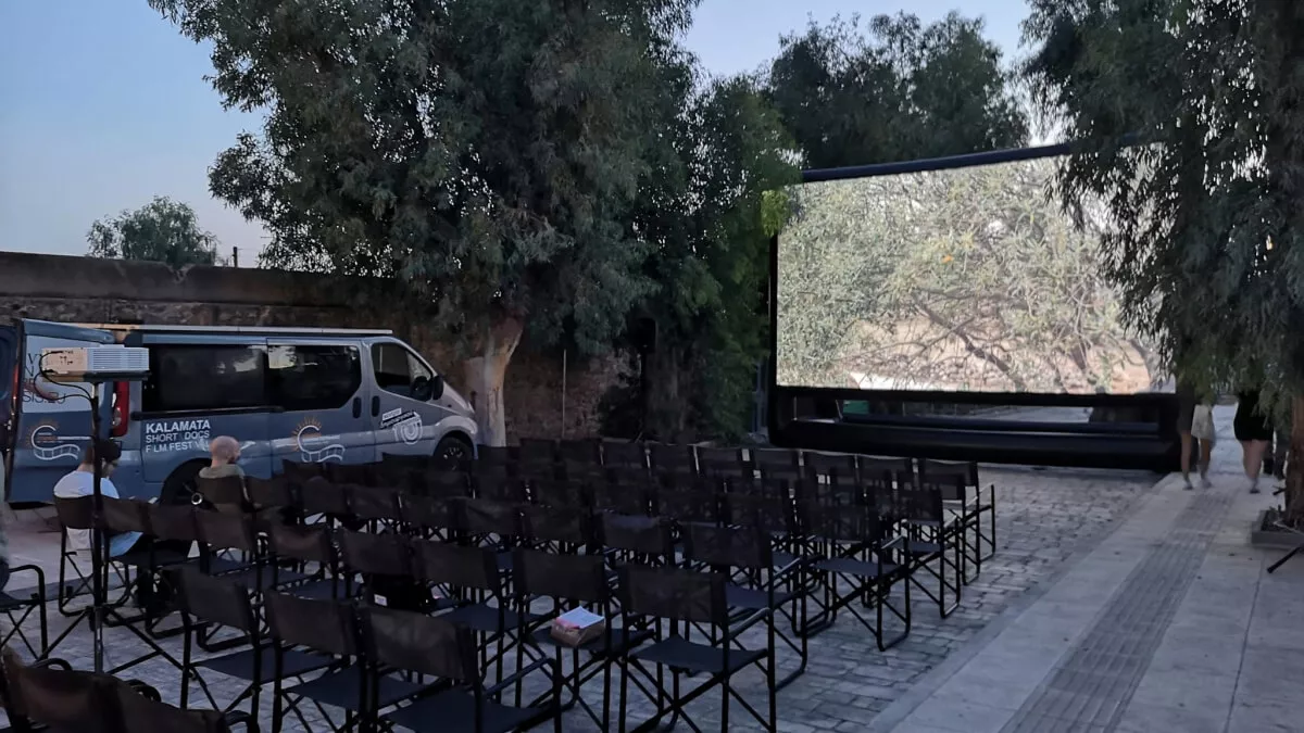 Προετοιμασία για υπαίθρια προβολή τη νύχτα. Μεγάλη φουσκωτή οθόνη στέκεται μπροστά από άδειες καρέκλες, προβάλλοντας μια εικόνα με δέντρα, κατά τη διάρκεια των τελευταίων ελέγχων πριν την έναρξη.